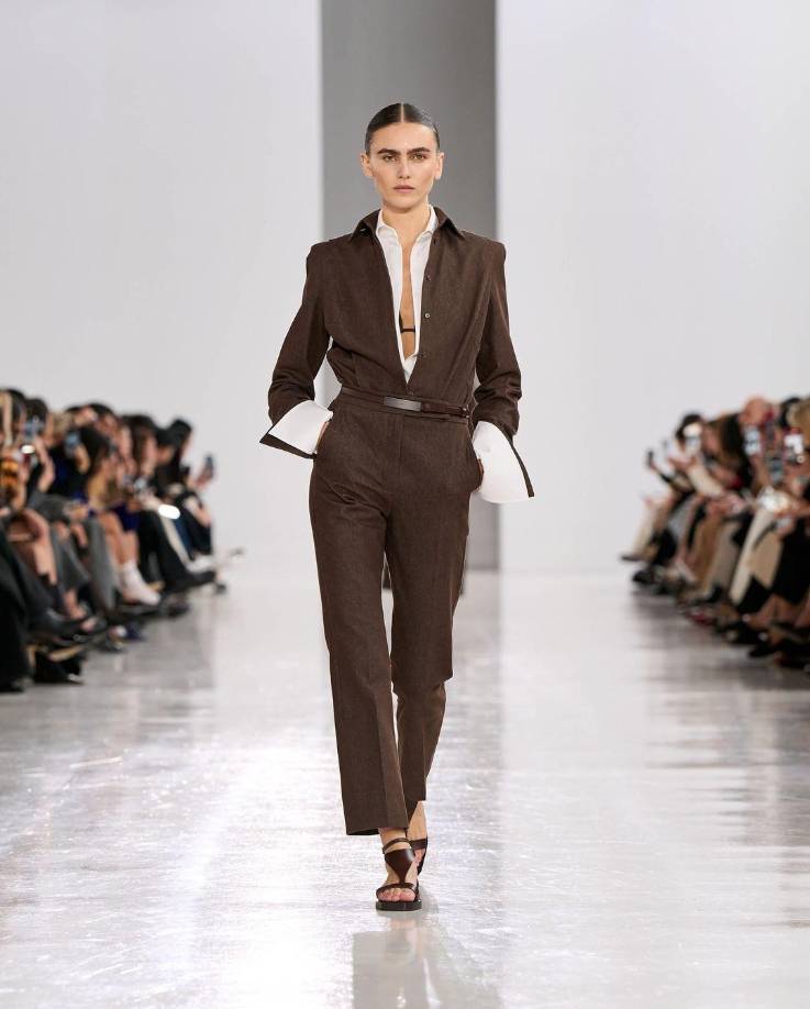 La modelo Vittoria Ceretti abrió el show con un conjunto ejecutivo en marrón, compuesto por una blusa desabotonada y sandalias de cuero, logrando un equilibrio entre formalidad y frescura, complementado con un maquillaje natural y un pulcro recogido que acentuaba la estética “clean-girl” .