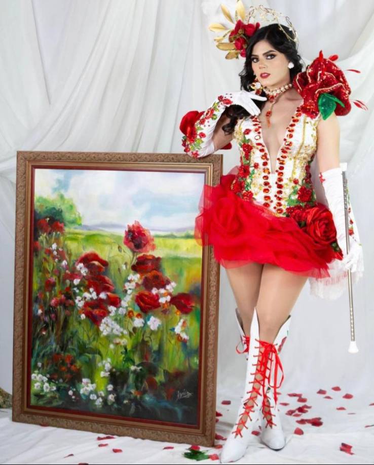 En la falda vuelos de punto rojo que simulan ser pétalos y decorados con rosas de tela de razo hechas a mano, el tocado armado sobre un arometálico complementado con plumas, perlas y rosas, la capa blanca con flecos y como punto final un par de blancas botas con ramos de rosaspintadas a mano.