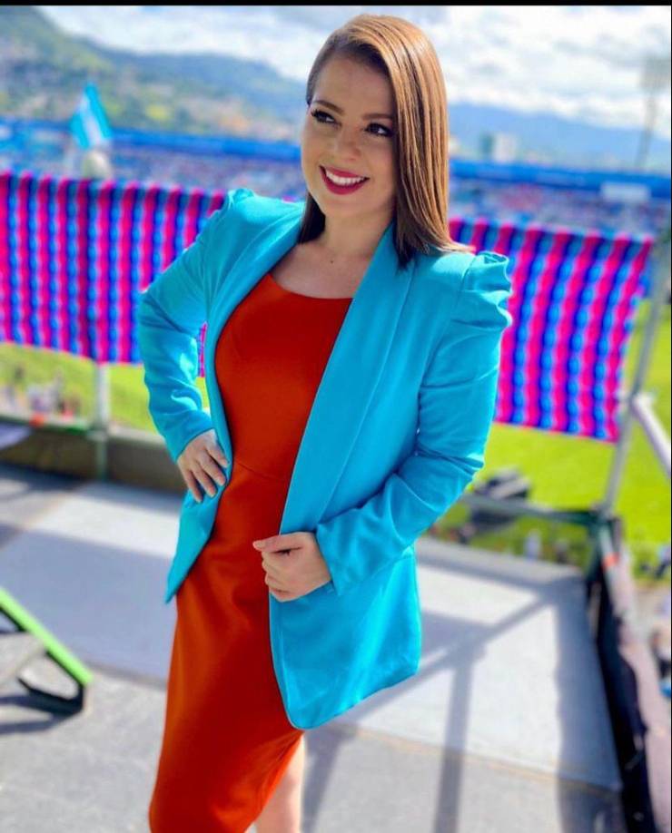Jacky Redondo de TSI luce un vestido color rojo acompañado con una chaqueta color azul turquesa. 