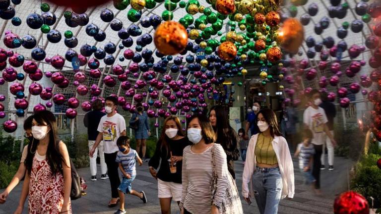 Personas que usan máscaras caminan debajo de las decoraciones afuera de un centro comercial en Bangkok cuando Tailandia registró el lunes su primer caso de la variante Omicron.