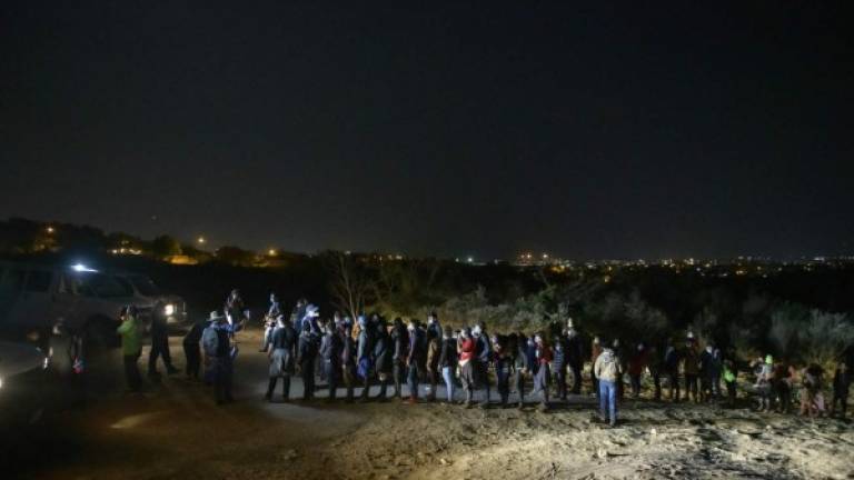 Immigrants who arrived illegally across the Rio Grande river from Mexico line up on March 27, 2021 at a processing checkpoint before being detained by border patrol agents in the border city of Roma. (Photo by Ed JONES / AFP)
