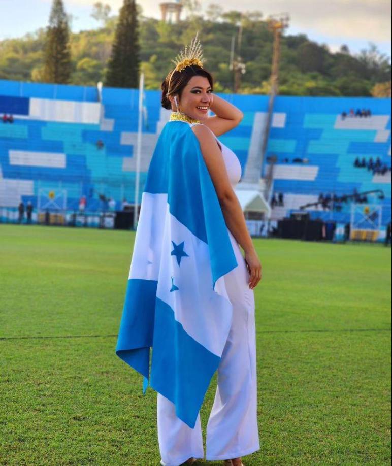 Milagro Flores de HCH luce un mono blanco con detalles dorados y una capa con la Bandera de Honduras. 