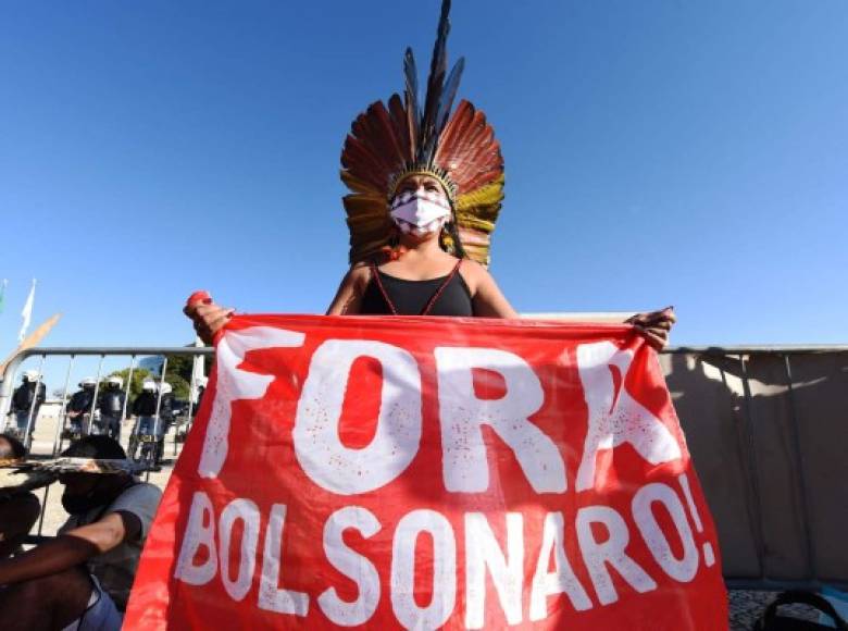 (FILES) In this file photo taken on June 30, 2021 An indigenous woman holds a sign reading Bolsonaro out, referring to Brazilian President Jair Bolsonaro, during a protest against a controversial land reform bill, outside the Supreme Court in Brasilia. - The Brazilian Articulation of Indigenous People (APIB) requested on Monday the International Criminal Court (ICC) to investigate President Jair Bolsonaro for his 'anti-indigenous policy', which they qualify as a 'genocide' and an 'ecocide'. (Photo by EVARISTO SA / AFP)