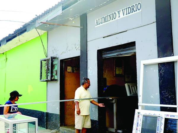 <b>Dos personas frente a un negocio que fabrica muebles y puertas de vidrio en San Pedro Sula.</b>
