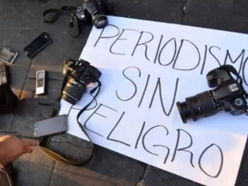 Cámaras fotográficas y teléfonos móviles descansan sobre una pancarta con la consigna “Periodismo sin peligro”, en una manifestación donde profesionales de la comunicación exigen garantías y protección para el libre ejercicio periodístico.