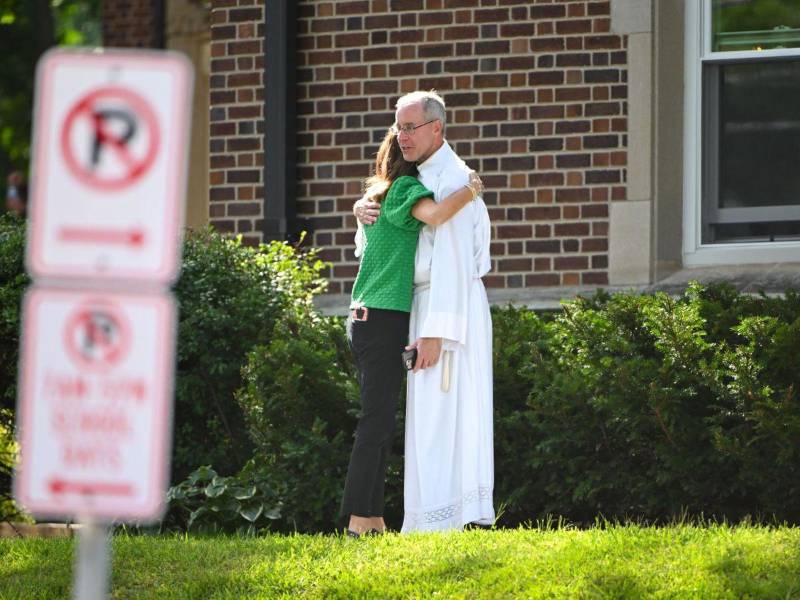 Una madre de familia abraza a un sacerdote en la escuela católica de la Anunciación, en Minneapolis, tras el ataque que dejó dos niños muertos y 17 personas heridas.