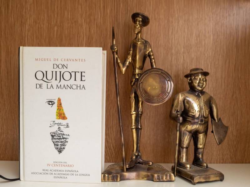 Un libro de Don Quijote de la Mancha (1605) al lado de una escultura dorada de bronce de don Quijote y de Sancho Panza.