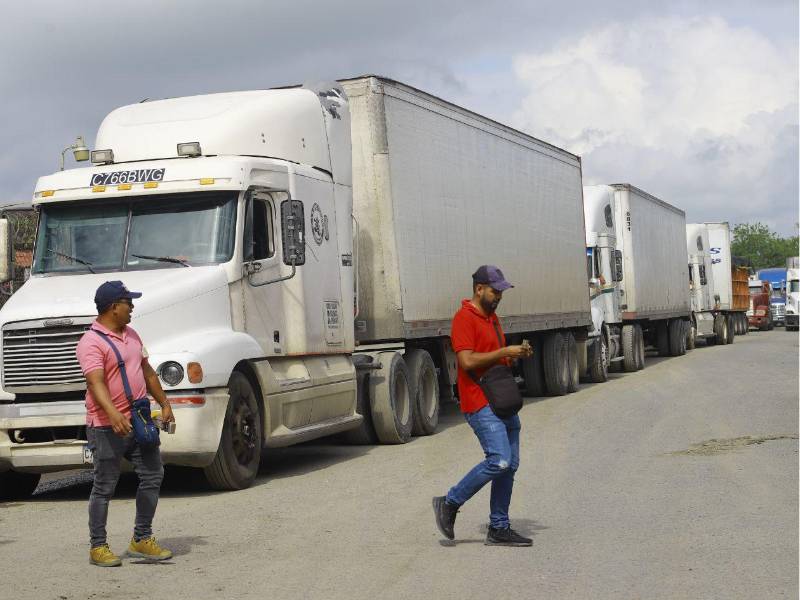 Cambistas de quetzales y lempiras caminan frente a una extensa fila de camiones estacionados en un carril de la carretera en la frontera de Corinto.
