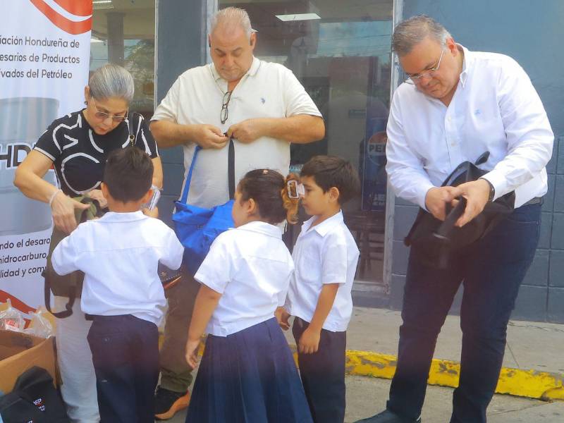 Olga Ayala, Wenceslao Lara y Jesús Yacamán entregan mochilas a niños de la escuela La Gran Familia de la colonia La Puerta en San Pedro Sula.