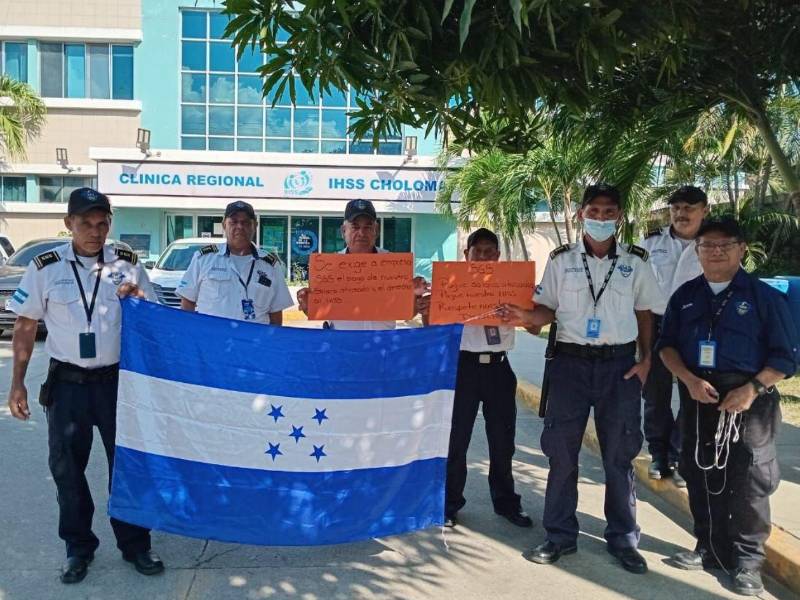 Guardias de seguridad del IHSS sostienen una bandera de Honduras y carteles donde exigen a la empresa contratante que les pague los salarios atrasados y respete el derecho a contar con un seguro médico.