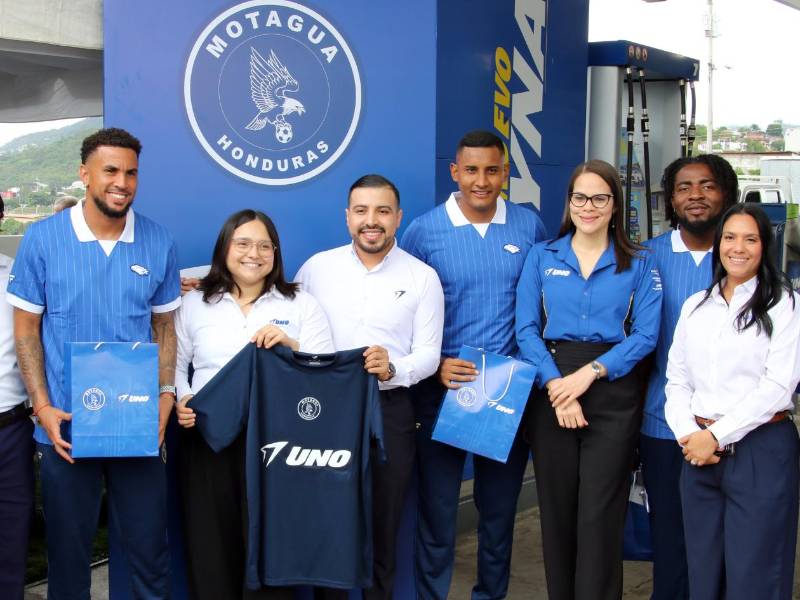 Jugadores del F.C. Motagua y colaboradores de Gasolineras UNO posan juntos en una de las estaciones de servicio de la marca, sosteniendo obsequios y la camiseta oficial del equipo.