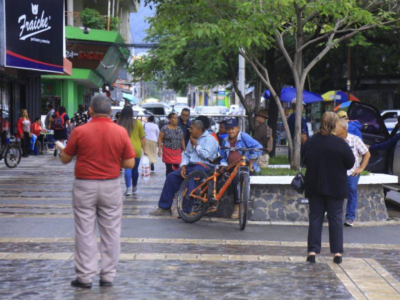 Sampedranos transitan por el parque central, mientras que un grupo de hombres descansan a la sombra de un árbol.