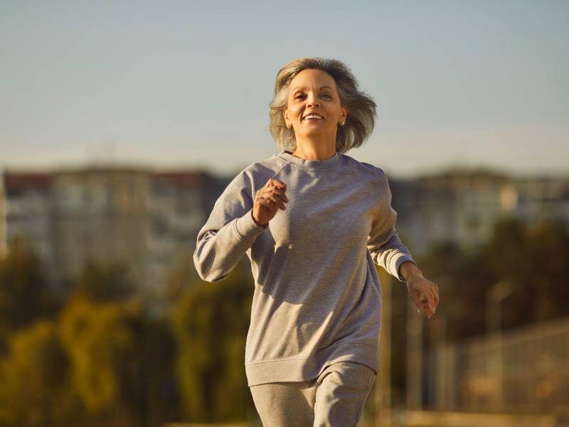 Mujer mayor sonriente en ropa deportiva que corre durante su entrenamiento.