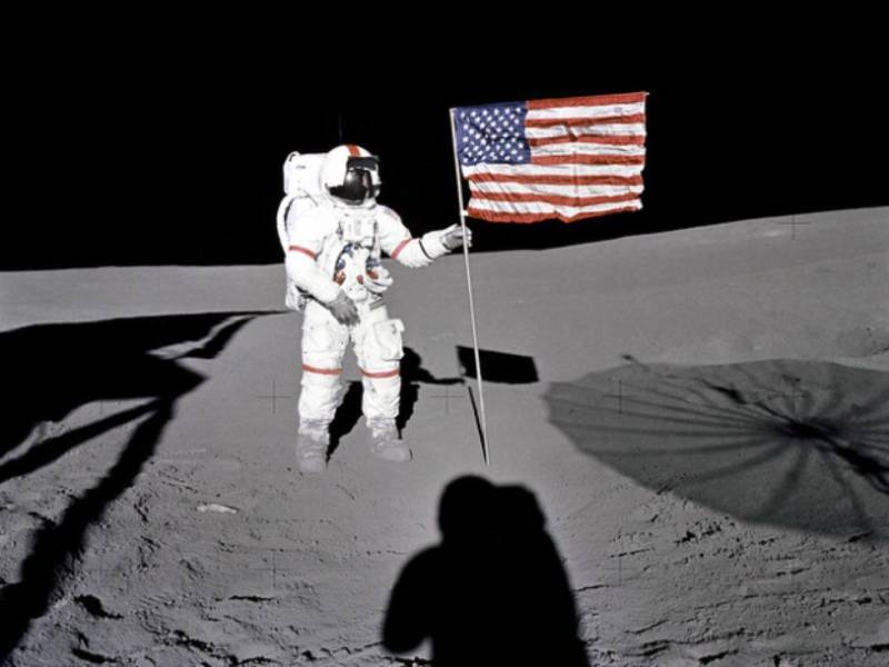 El astronauta Alan B. Shepard Jr., comandante del Apollo 14, se encuentra junto a la bandera de Estados Unidos en las tierras altas de Fra Mauro, en la Luna, durante los primeros momentos de la primera actividad extravehicular (EVA-1) de la misión. Las sombras del módulo lunar “Antares”, del astronauta Edgar D. Mitchell, piloto del módulo lunar, y de la antena S-band desplegable rodean la escena de la tercera colocación de una bandera estadounidense en la superficie lunar.
