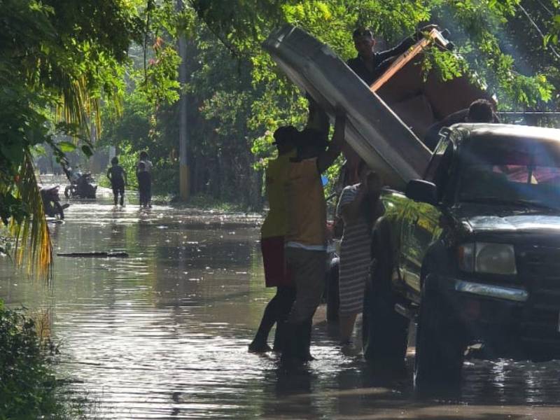 Personal de bomberos ayudan a familias de La Duarte a sacar algunos de sus enseres del hogar.