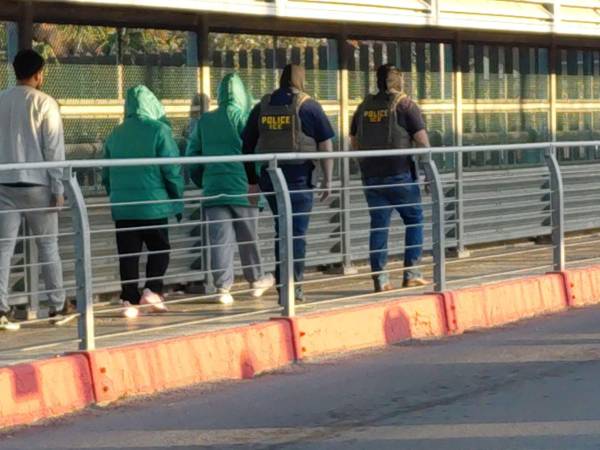 Un grupo de migrantes es llevado por el puente internacional McAllen-Hidalgo por un grupo de agentes del Servicio de Inmigración y Control de Aduanas de Estados Unidos (ICE, por sus siglas en inglés).