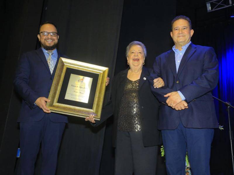 Martha Abarca recibiendo su distinción Esencia de Mujer, tomada del brazo de su hijo, John Stainer.