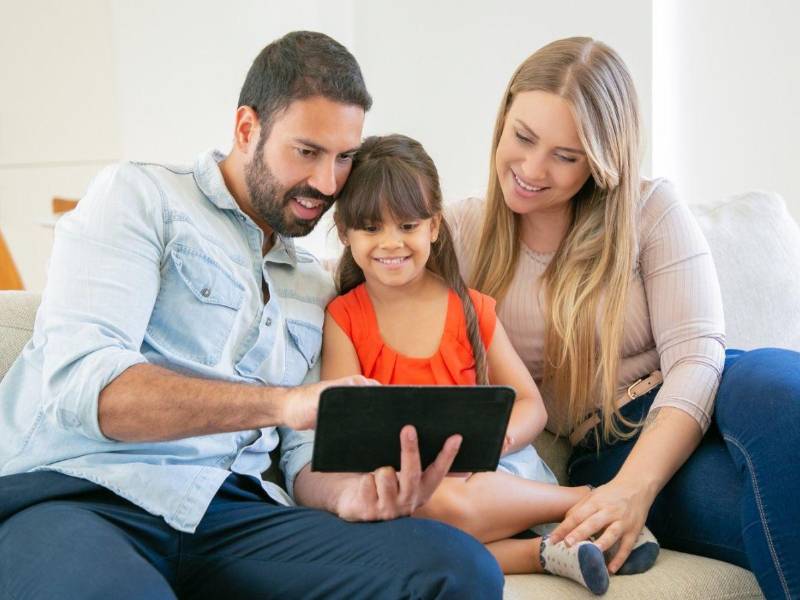 Dos adultos muestran a su hija como utilizar las herramientas digitales sin caer en riesgos.