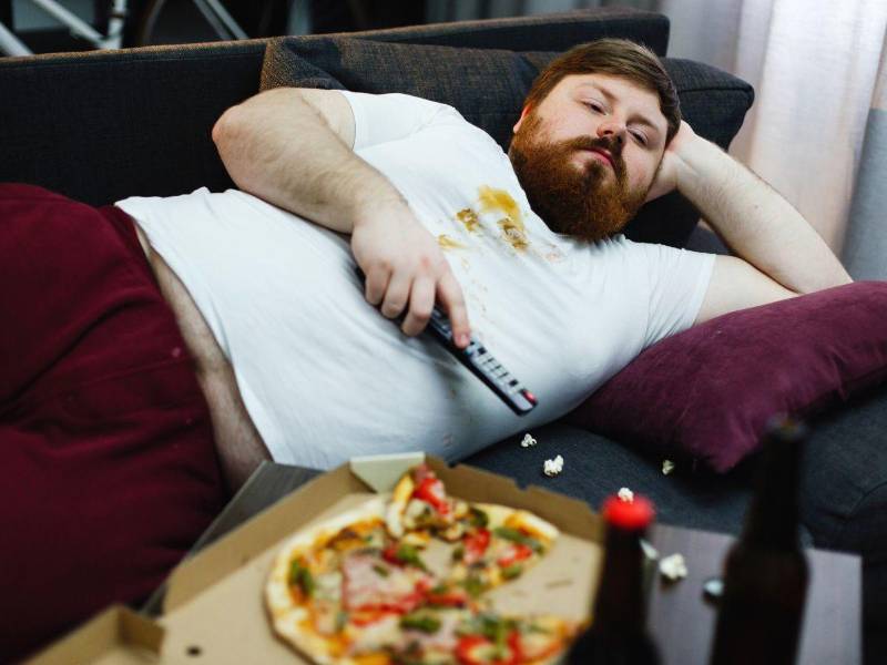 Un joven consume comida rápida y bebidas azucaradas mientras ve televisión.