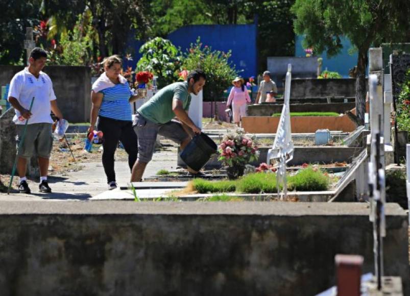 Un hombre riega las plantas de una tumba en el cementario La Puerta de San Pedro Sula.