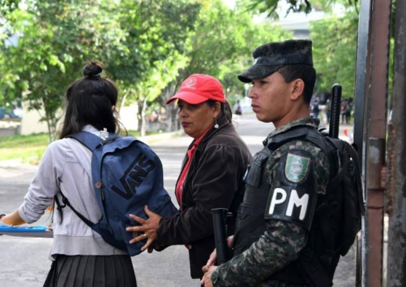 A guard checks a students' backpack as a Military Police agent guards the Vicente Caceres Institute in Tegucigalpa on July 18, 2017.<br/><br/>The institute is being guarded by Honduran national police agents and members of the Military Police due to gang harassment. According to the National Autonomous University of Honduras (UNAH), 33 students were killed in the first semester of 2017. / AFP PHOTO / ORLANDO SIERRA / TO GO WITH AFP STORY BY NOE LEIVA