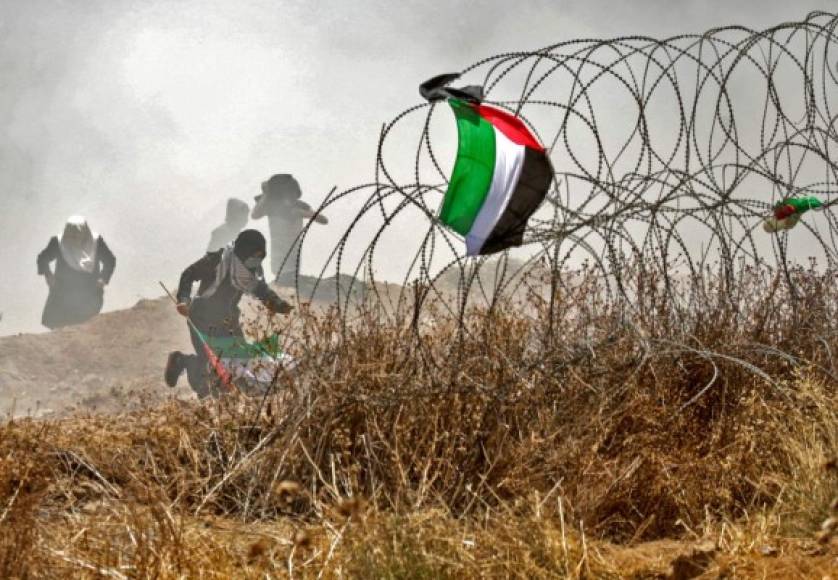La bandera palestina ondea sobre una alambrada mientras la gente corre detrás de ella.