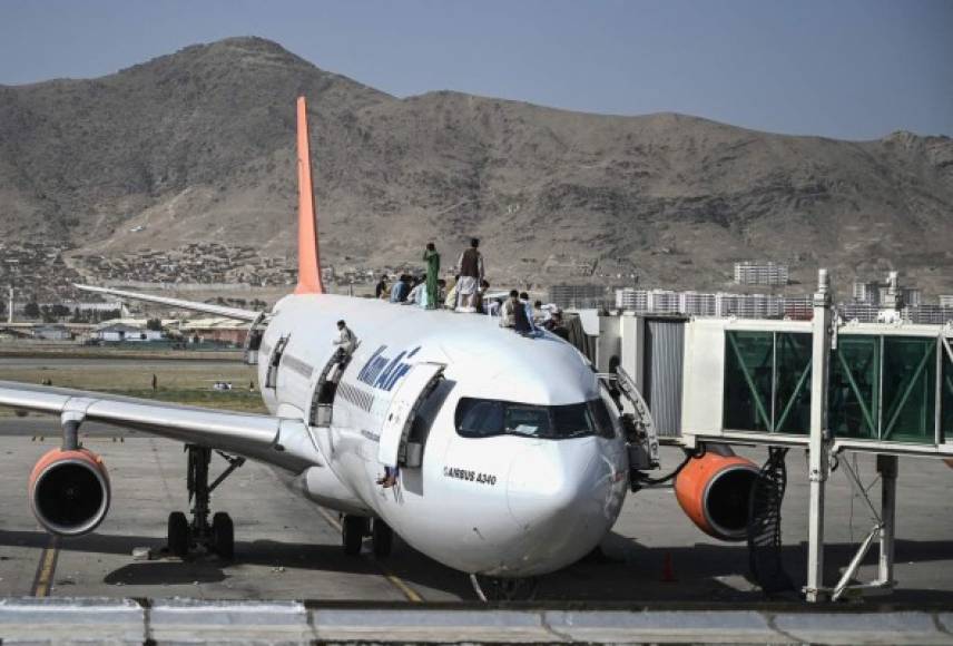 Afghan people climb atop a plane as they wait at the Kabul airport in Kabul on August 16, 2021, after a stunningly swift end to Afghanistan's 20-year war, as thousands of people mobbed the city's airport trying to flee the group's feared hardline brand of Islamist rule. (Photo by Wakil Kohsar / AFP)