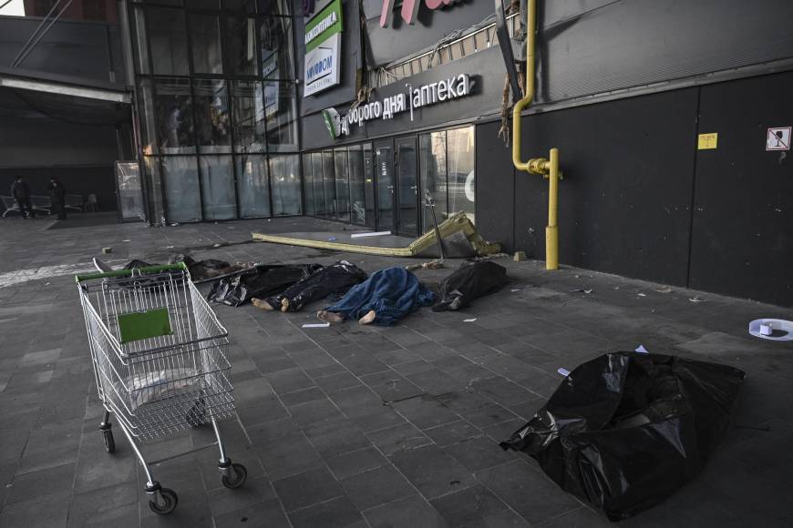 Bajo un toldo del que cuelgan grandes carteles publicitarios, seis cadáveres yacen en el suelo con sus pies desnudos sobresaliendo del plástico negro con el que se les ha recubierto. 