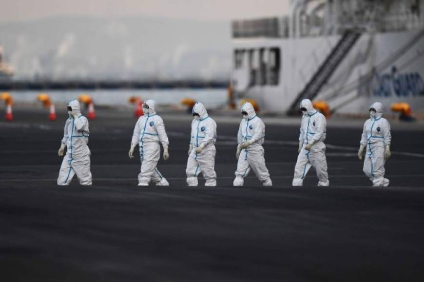 TOPSHOT - People wearing protective suits walk from the Diamond Princess cruise ship, with around 3,600 people quarantined onboard due to fears of the new coronavirus, at the Daikoku Pier Cruise Terminal in Yokohama port on February 10, 2020. - Around 60 more people on board the quarantined Diamond Princess cruise ship moored off Japan have been diagnosed with novel coronavirus, the country's national broadcaster said on February 10, raising the number of infected passengers and crew to around 130. (Photo by CHARLY TRIBALLEAU / AFP)