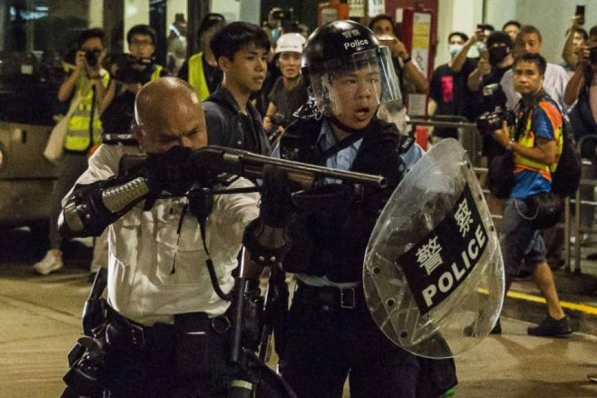 A police officer (L) points a firearm during a clash with protesters who had gathered outside Kwai Chung police station, in support of protesters detained with the charge of rioting, in Hong Kong late on July 30, 2019. - Renewed clashes broke out between pro-democracy protesters and police in Hong Kong late on July 30 after dozens of demonstrators were charged with rioting -- an offence that carries a jail term of up to ten years. (Photo by ISAAC LAWRENCE / AFP)