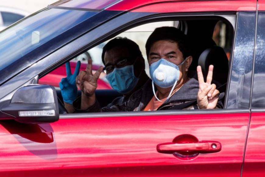 Dos hombres con máscaras faciales y esperando en su automóvil señalan el signo de la victoria durante una distribución de alimentos de Pascua en el Honda Center en medio de la pandemia de coronavirus en Anaheim, al sur de Los Ángeles. EFE