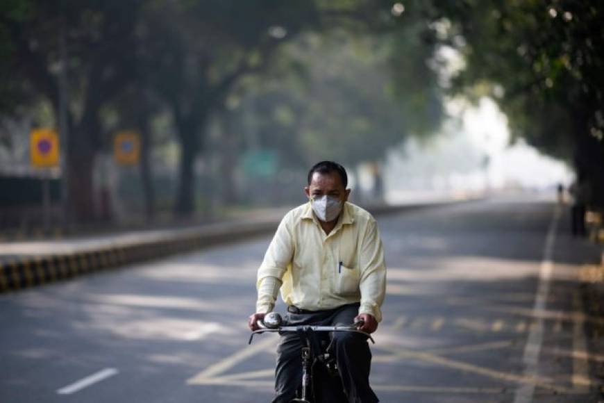Un hombre que usa una máscara facial como medida preventiva contra el coronavirus COVID-19 monta su bicicleta a lo largo de una calle vacía en Nueva Delhi. Foto AFP