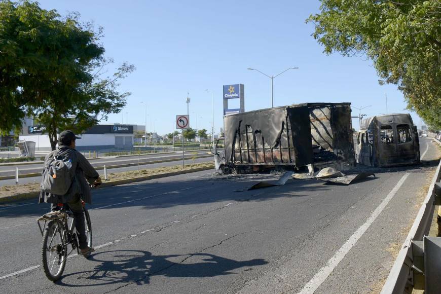  Una persona transita con su bicicleta frente a vehículos calcinados hoy, tras los enfrentamientos de fuerzas federales con grupos armados, en la ciudad de Culiacán, estado de Sinaloa (México).
