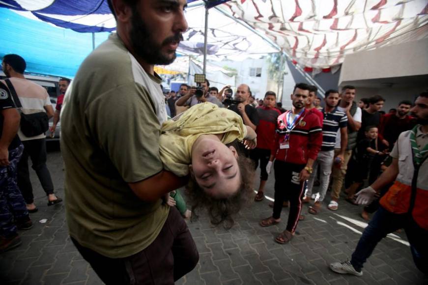 Un hombre corre mientras lleva a un niño pequeño al hospital Al-Shifa tras el bombardeo de una casa durante el bombardeo israelí del barrio Mansura de la ciudad de Gaza.