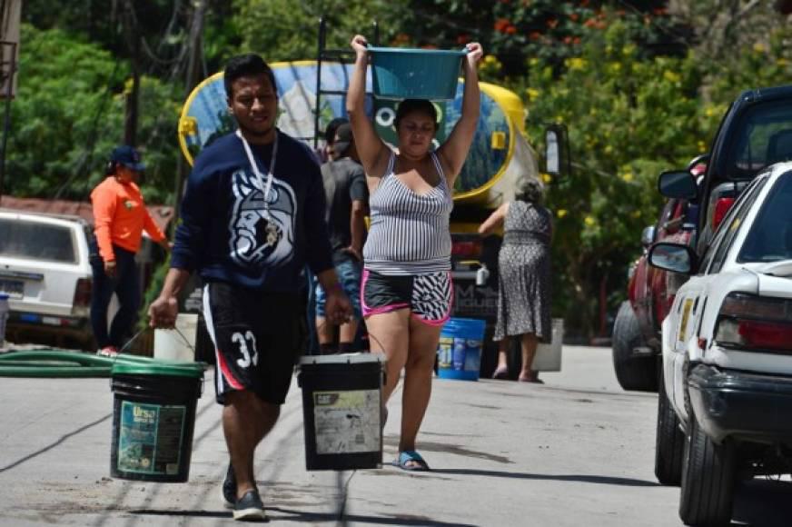 Ciudadanos acarrean agua en cubetas en una colonia de Tegucigalpa. Atrás la cisterna que los abastece.