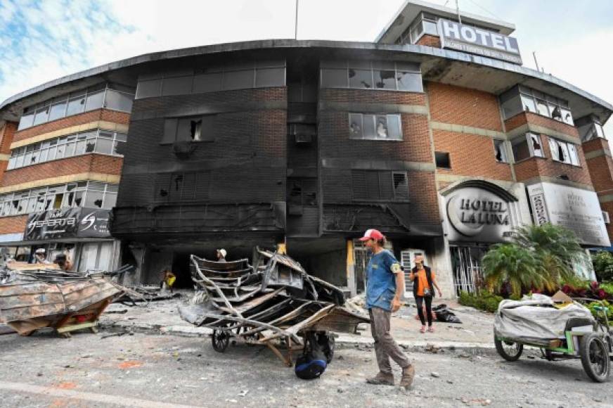 People take out scrap metal from hotel burned last night during clashes between demonstrators and riot police officers in the protests against the government's tax reform in Cali, Colombia, on May 4, 2021. - The international community on Tuesday decried what the UN described as an 'excessive use of force' by security officers in Colombia after official data showed 19 people were killed and 846 injured during days of anti-government protests. (Photo by LUIS ROBAYO / AFP)