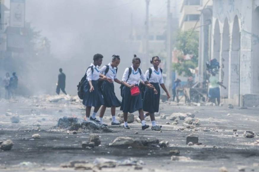HAITÍ. A la escuela entre humo de protestas. Niñas en uniforme caminan por la calle durante una manifestación en Puerto Príncipe; ciudadanos protestaronn contra el incremento de impuestos.
