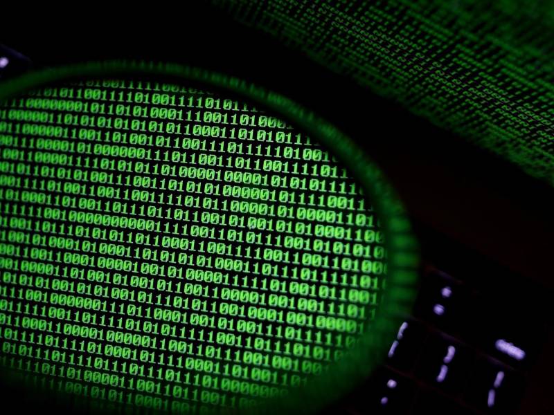 Un espejo refleja una pantalla de ordenador que muestra un código binario.