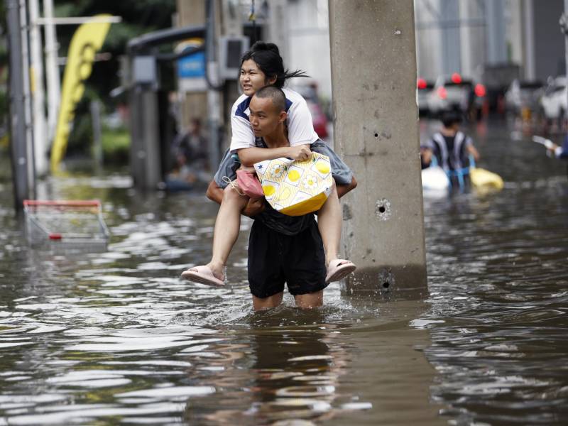 Un hombre lleva a una mujer a cuestas mientras camina por una calle anegada en el distrito de Bangkapi, en la capitalina Bangkok, declarada zona de desastre por inundaciones tras persistentes y fuertes lluvias. EFE/EPA/RUNGROJ YONGRIT