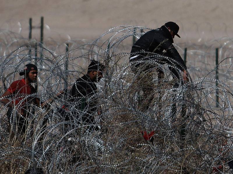 Migrantes intentan cruzar la cerca de alambres en la frontera que divide a México de los Estados Unidos en Ciudad Juárez (México).