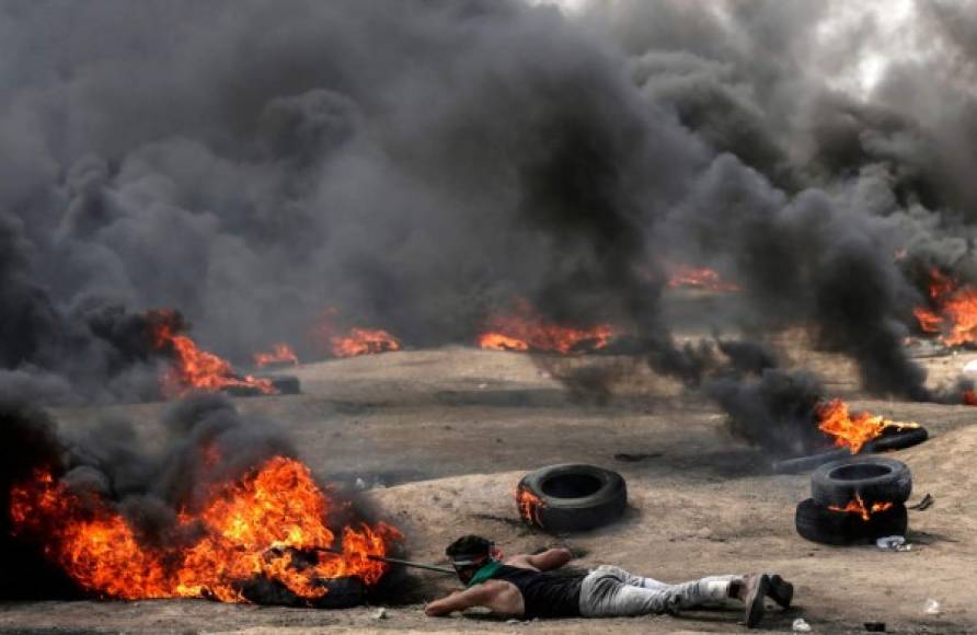 Un joven palestino empuja un neumático en llamas mientras yace tendido pecho a tierra.