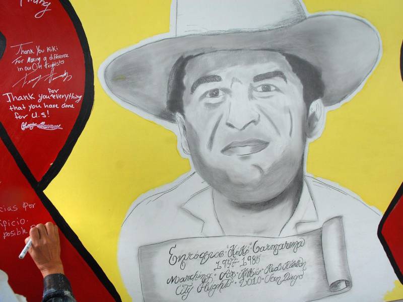 Fotografía de archivo de una mujer que escribe un mensaje sobre un mural con el rostro de Enrique Kiki Camarena.