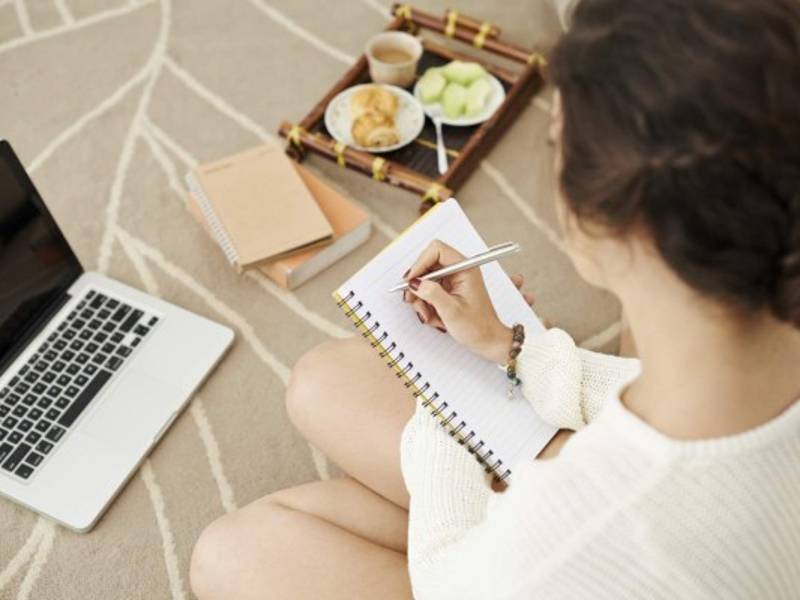 Female student sitting on the floor and making notes, view over the shoulder
