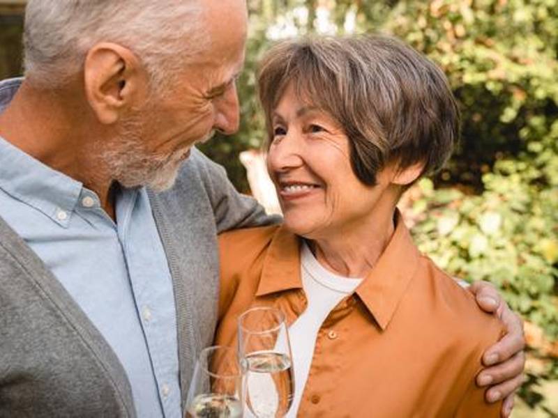 Alegre pareja de ancianos, esposos y abuelos abrazándose mientras celebran un aniversario especial con vino y champán al aire libre en el parque
