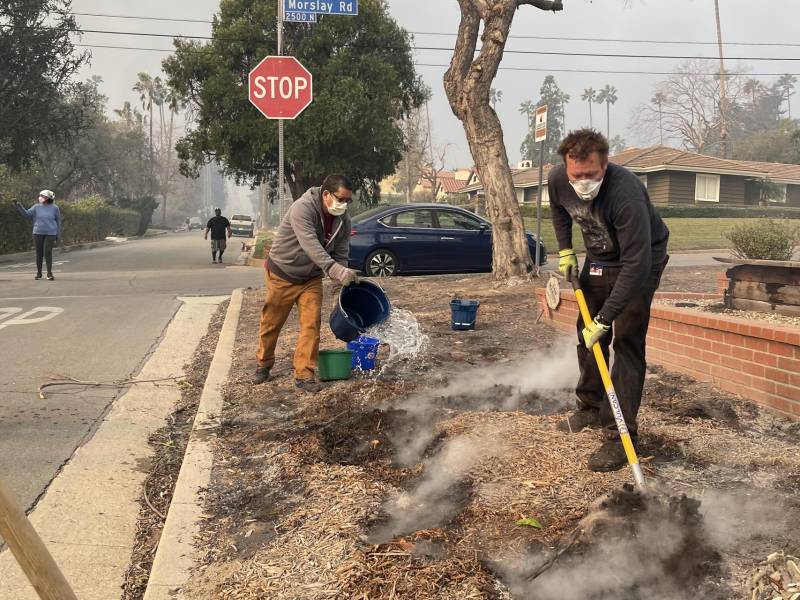 Unas personas vierten agua alrededor de las casas de un vecindario en Altadena, California (Estados Unidos).