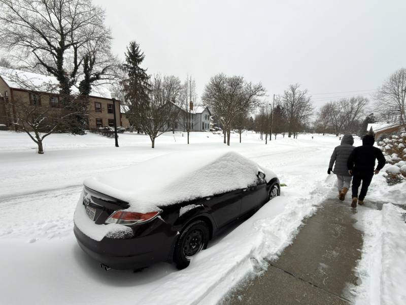 Dos personas caminan al lado de una calle afectada por la nieve este domingo en la ciudad de Hudson, Ohio (EE.UU.).
