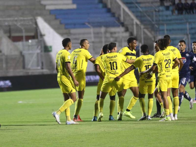 Jorge Serrano en el suelo mientras futbolista de Real España reclaman al árbitro Nelson Salgado.