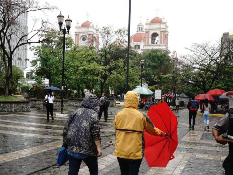 Hondureños se cubren de la lluvia en San Pedro Sula.