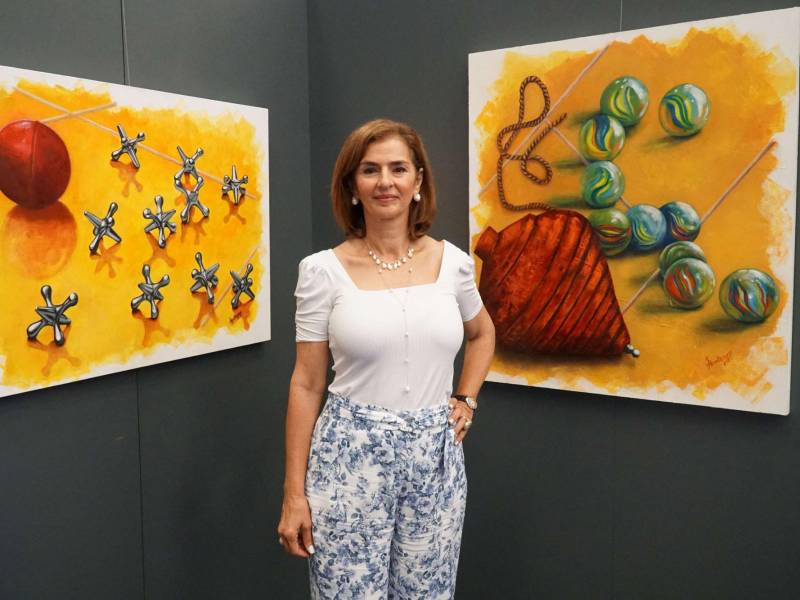 Suyapa Monterroso junto a sus dos obras que aluden a los juegos típicos de antaño, el trompo, los “maules” y los “yaxes”.