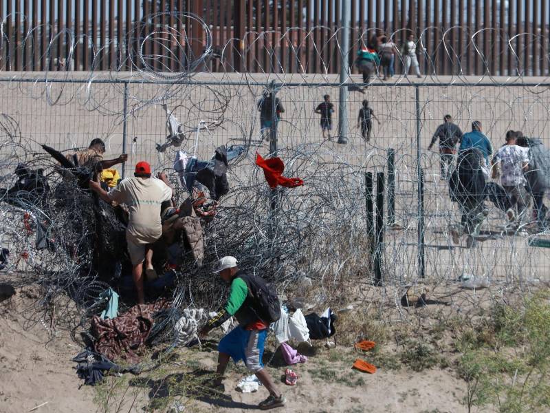 Migrantes cruzan una alambrada de navajas y púas, en la frontera que divide a México de los Estados Unidos, el 14 de marzo de 2024, en Ciudad Juárez (México).